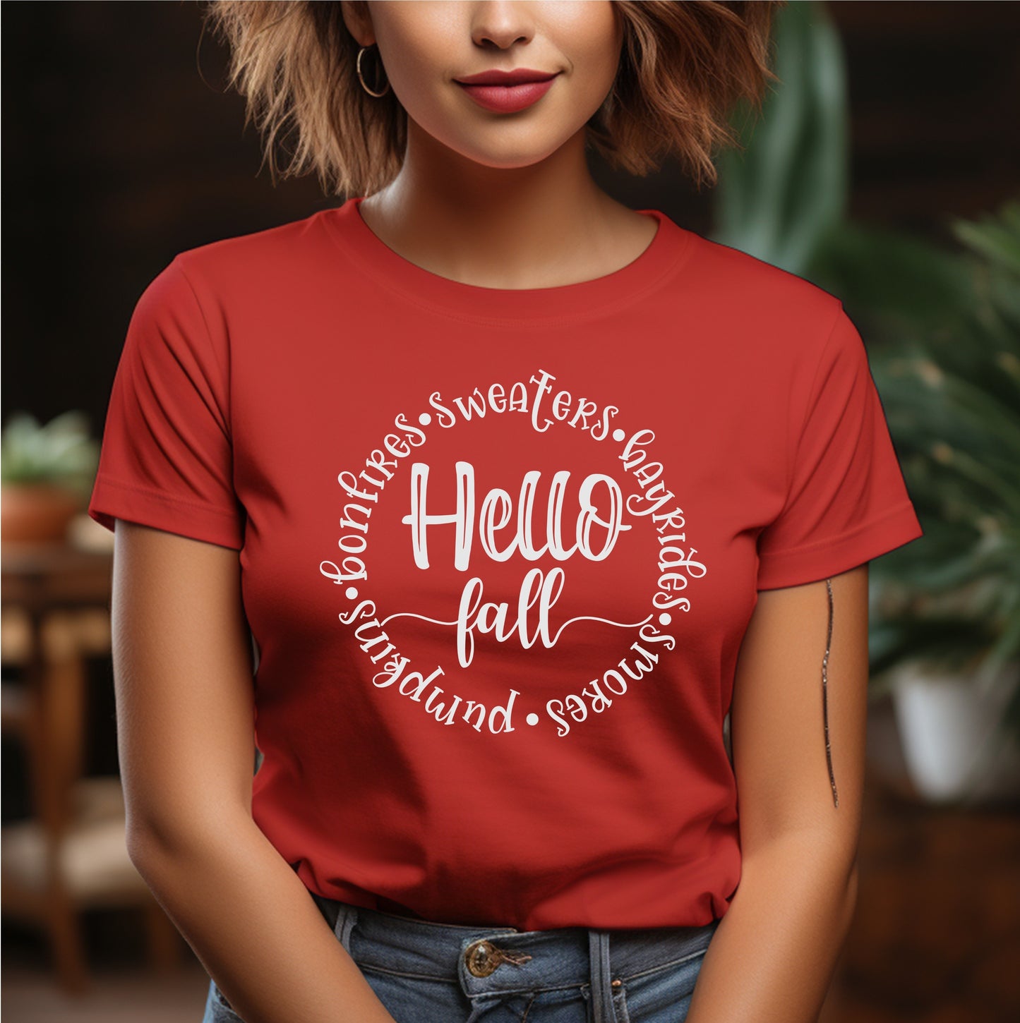 Woman wearing a red t-shirt with the phrase “Hello Fall” surrounded by seasonal words like bonfires, sweaters, hayrides, s’mores, and pumpkins in white script font.