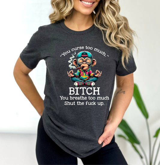 Woman wearing a dark gray Gildan T-shirt with a colorful meditating cartoon monkey smoking, surrounded by the text “You curse too much. Bitch. You breathe too much. Shut the fuck up.” in white lettering.