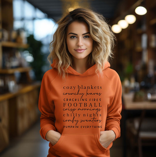 Orange fall hoodie with autumn quotes design – cozy blankets, crunchy leaves, pumpkin everything – worn by woman indoors