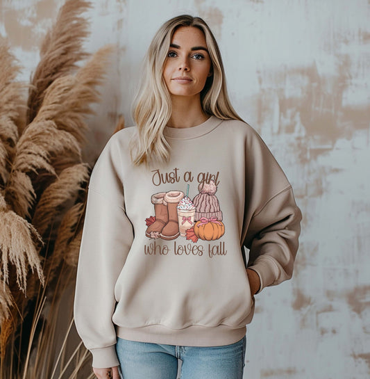 Woman wearing a neutral beige ‘Just a Girl Who Loves Fall’ sweatshirt with a cozy autumn graphic of boots, coffee, beanie, pumpkins, and leaves — perfect fall outfit for women